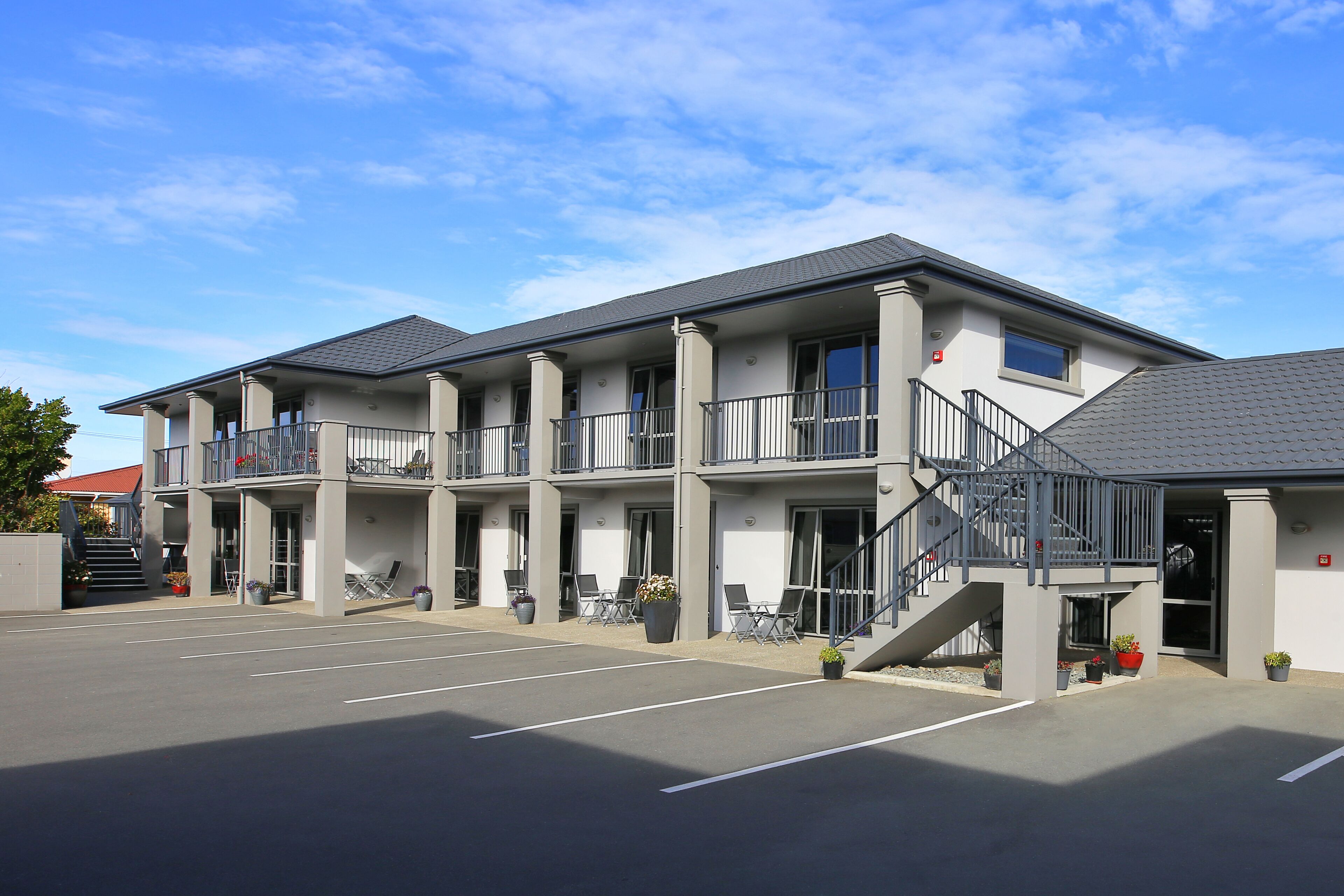 Un hôtel à plusieurs étages doté de balcons, d’un parking et d’un espace extérieur aménagé pour s’asseoir.