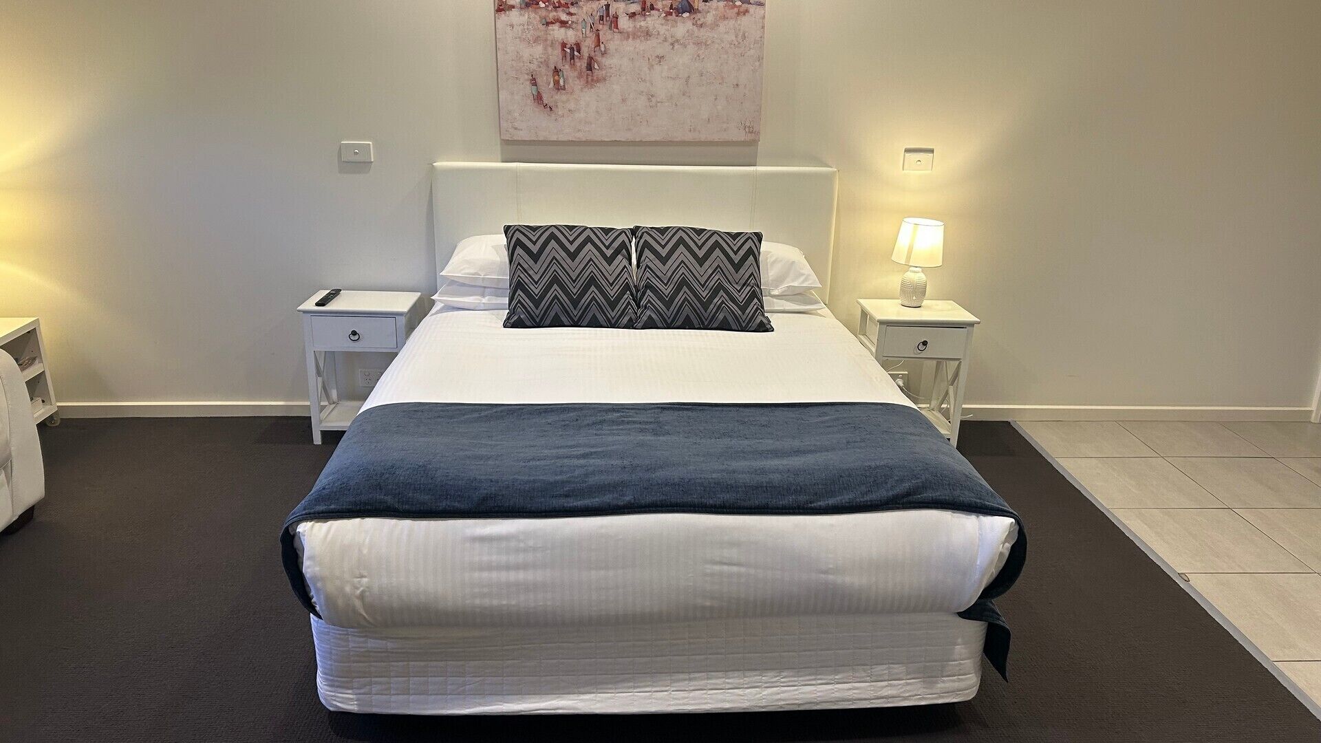 Een hotelkamer met een bed, twee nachtkastjes, een lamp en een schilderij aan de muur.