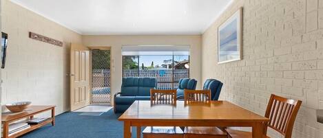 A room with a wooden dining table and chairs, a blue sofa, and a view of the outdoors through a glass door.