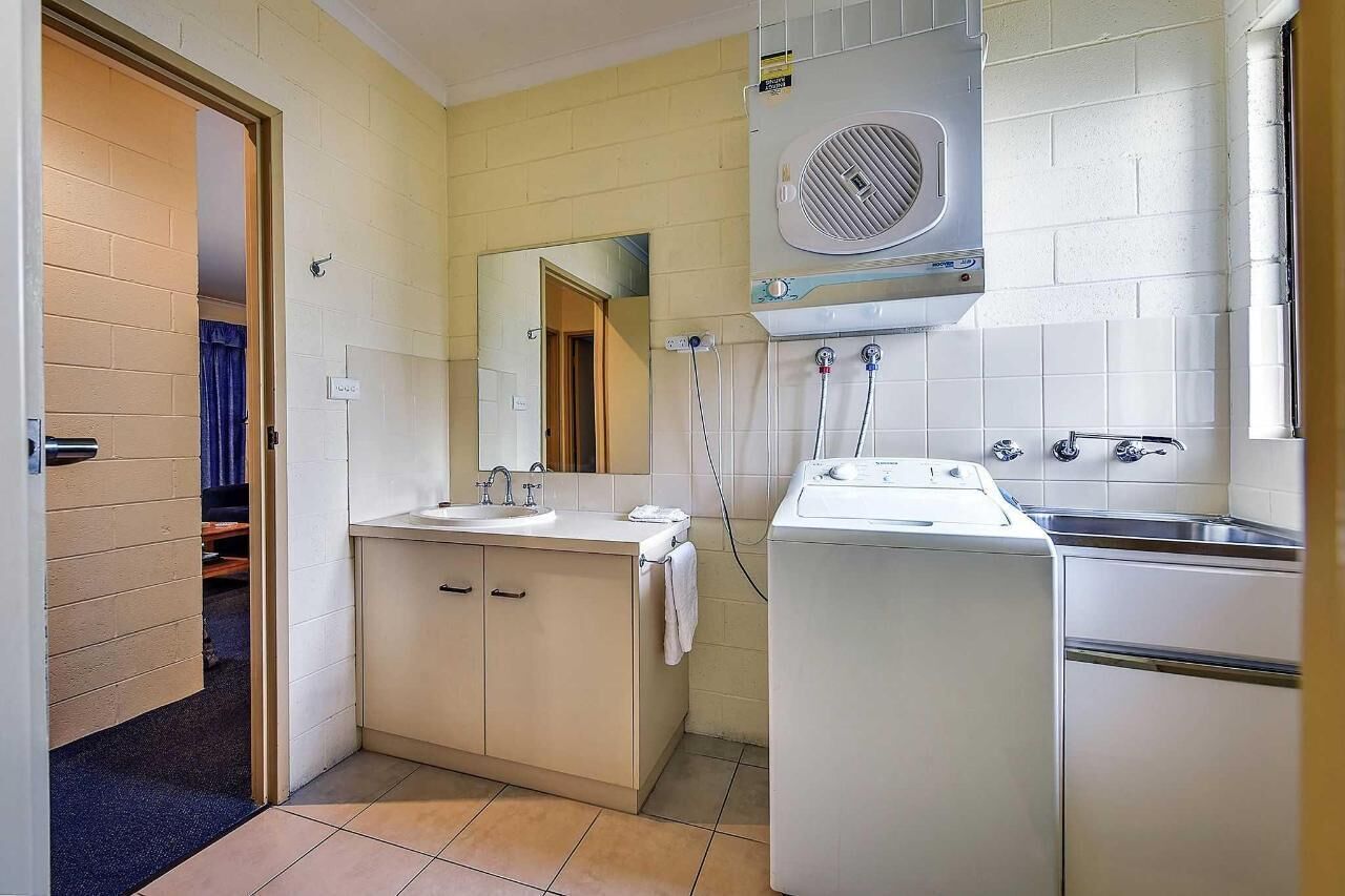 Een kleine badkamer met een wastafel, spiegel en een ingebouwde wasmachine.