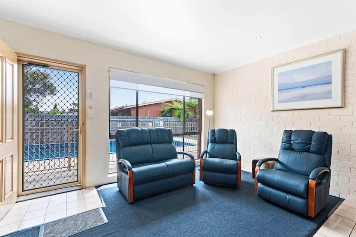 A room with three leather armchairs, a large window, and a framed picture on the wall.