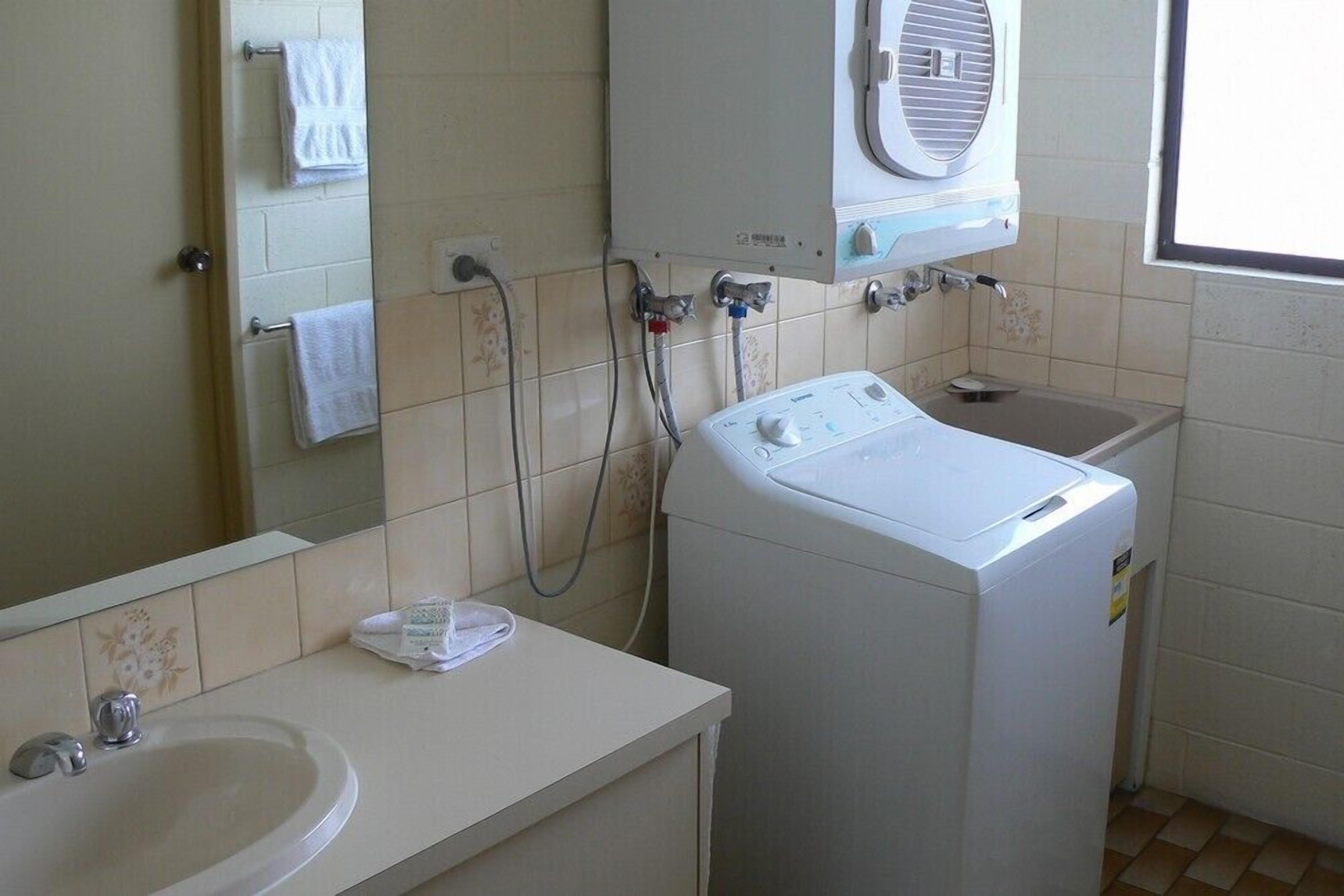 A bathroom with a sink, a mirror, a washing machine, and a window.