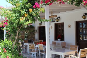 An outdoor seating area with white tables and chairs, surrounded by lush greenery and vibrant flowers. - Mare Monte (Ios)