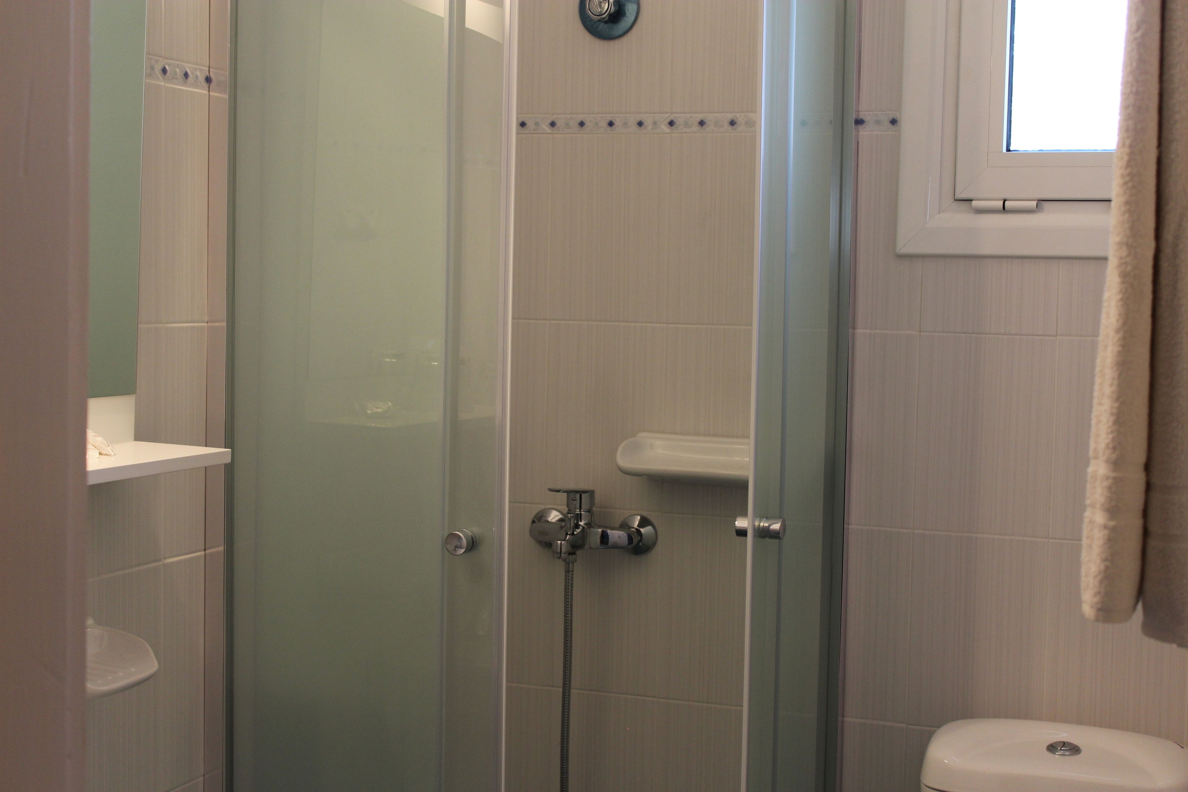 A glass-enclosed shower with a handheld showerhead, a wall-mounted faucet, and a small window above the toilet.