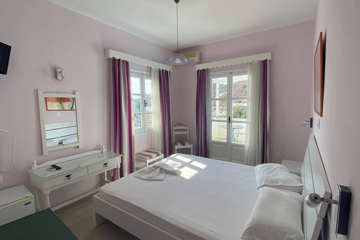 A bedroom with a bed, a bedside table, a chair, a dresser, a mirror, a TV, and a window with curtains.