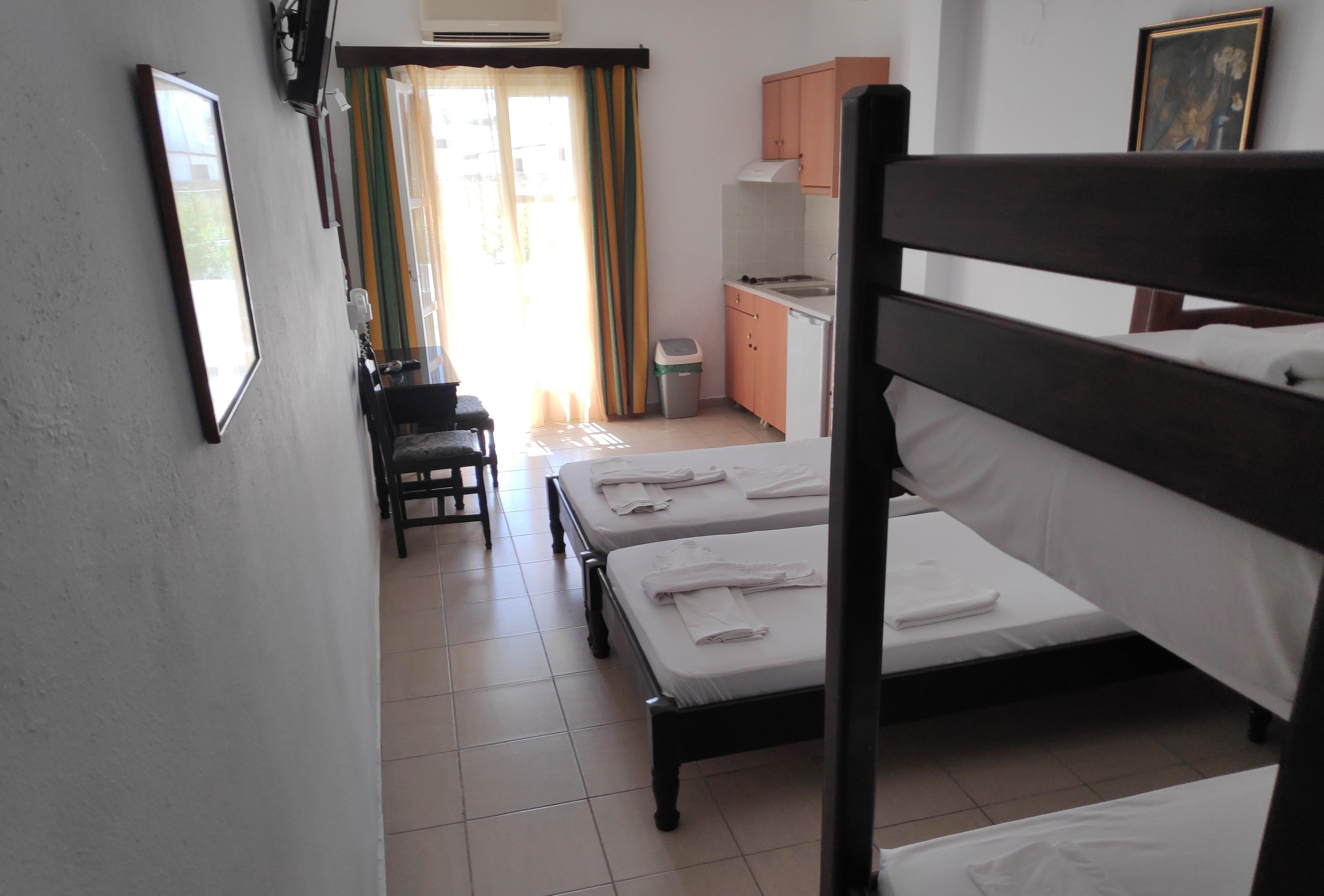 A hotel room with two beds, a small kitchenette, a desk, and a chair.