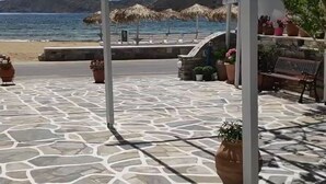 A stone-paved area with a bench and potted plants, overlooking a body of water and a beach. - Mare Monte (Ios)