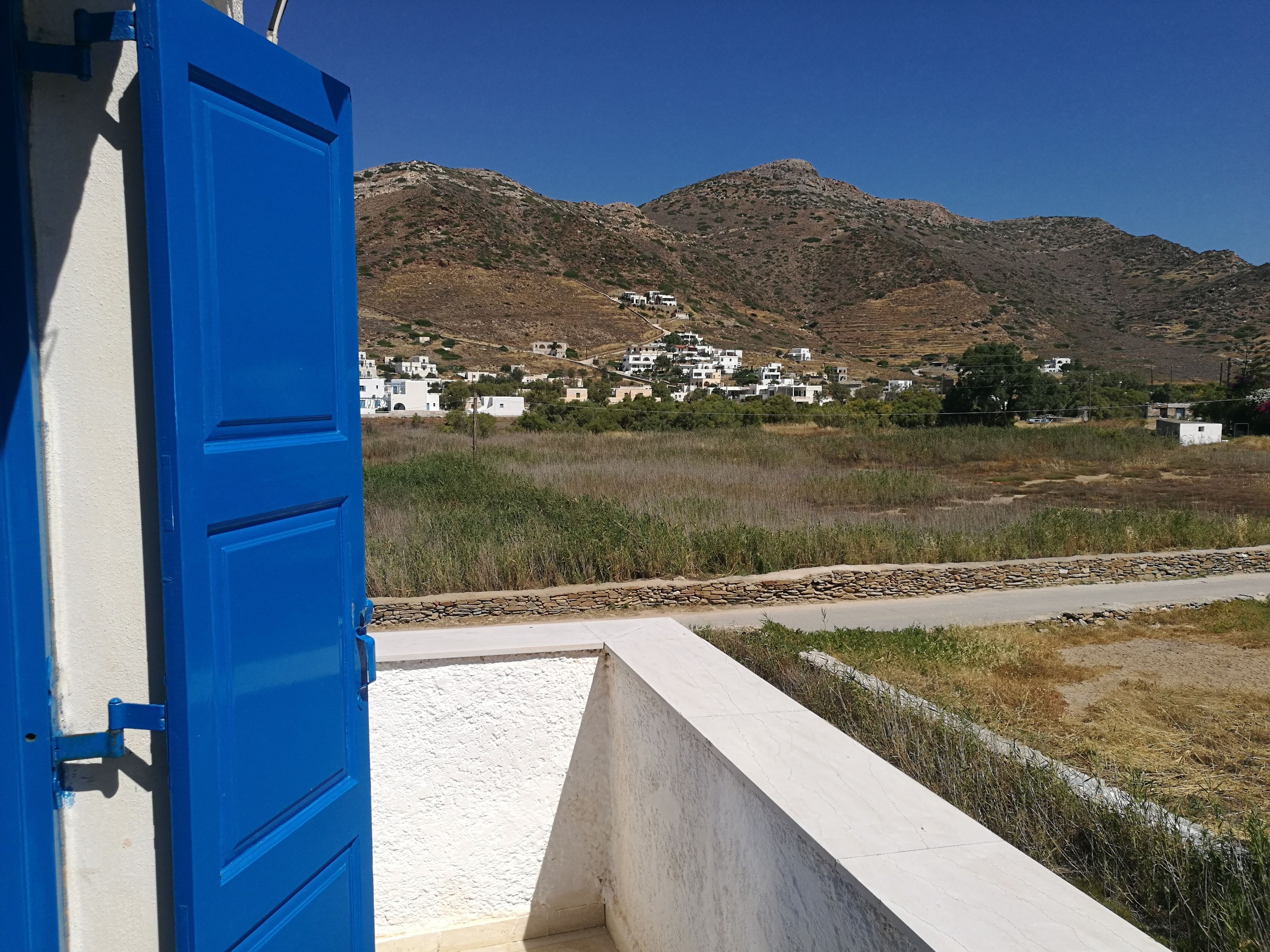 Un village côtier aux bâtiments blancs, avec une porte bleue et une montagne en arrière-plan.