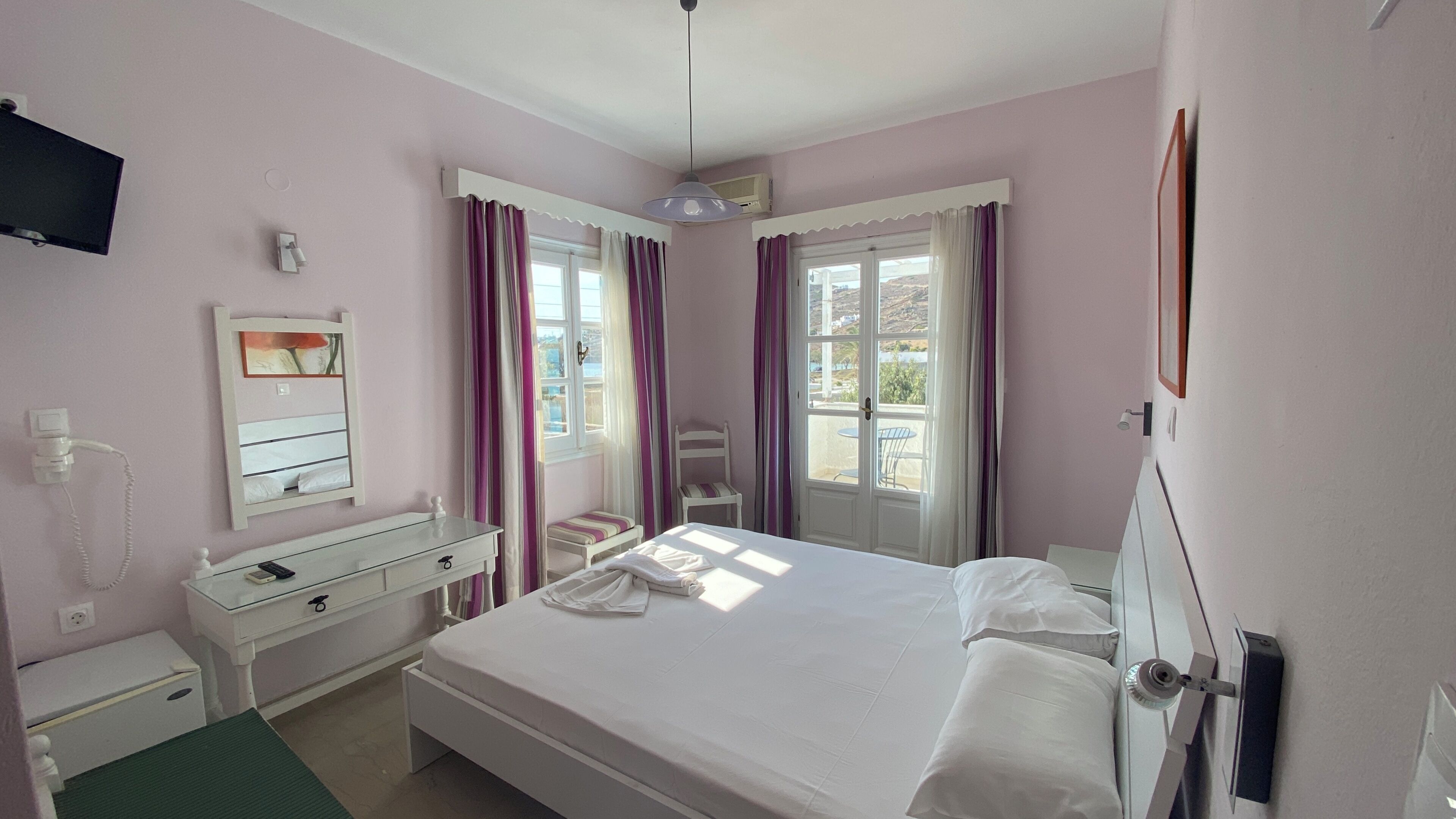 A bedroom with a bed, a bedside table, a chair, a dresser, a mirror, a TV, and a window with curtains.