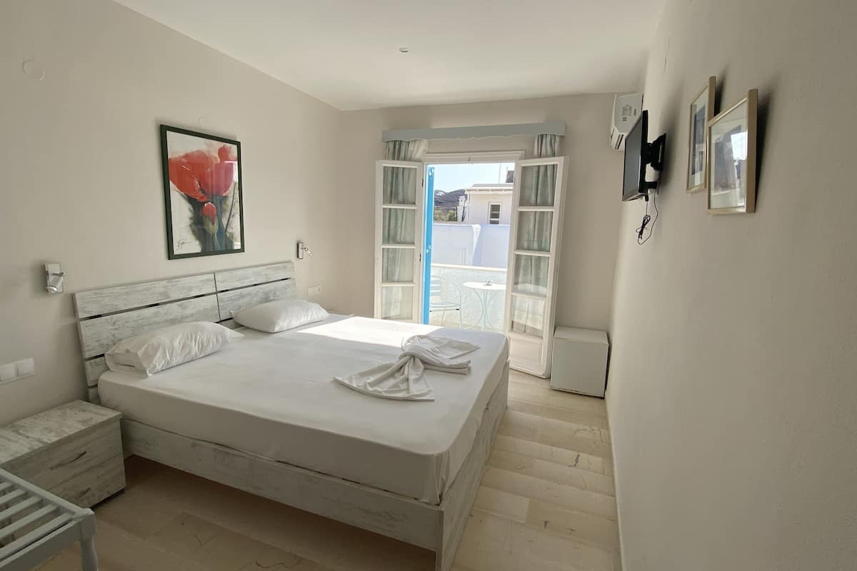 A bedroom with a bed, a nightstand, a radiator, a painting, and a view of the outside.