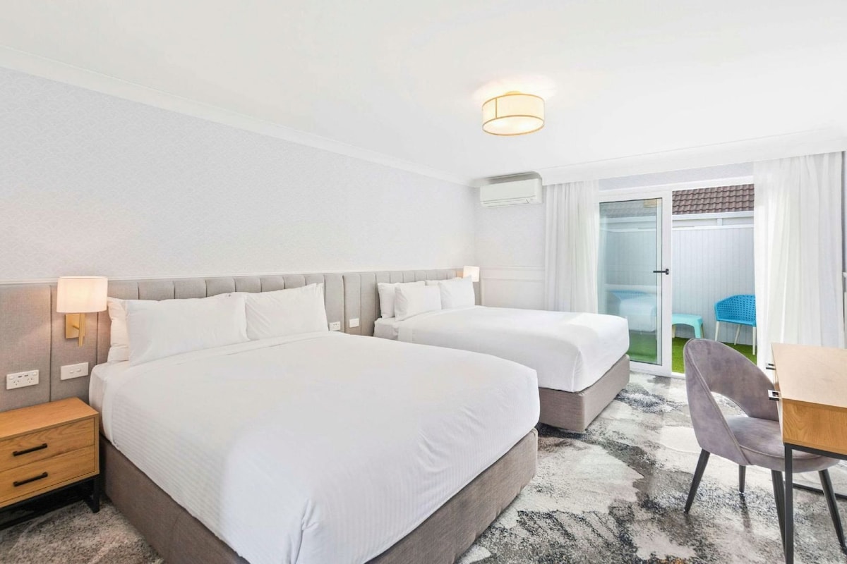 A hotel room with two beds, a desk, and a chair.