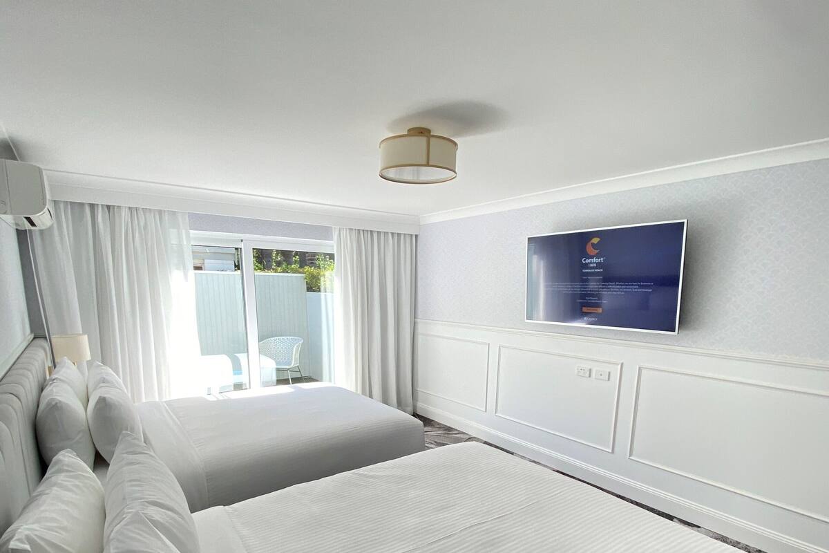 Une chambre d’hôtel avec deux grands lits, un téléviseur à écran plat fixé au mur et une fenêtre avec des rideaux.