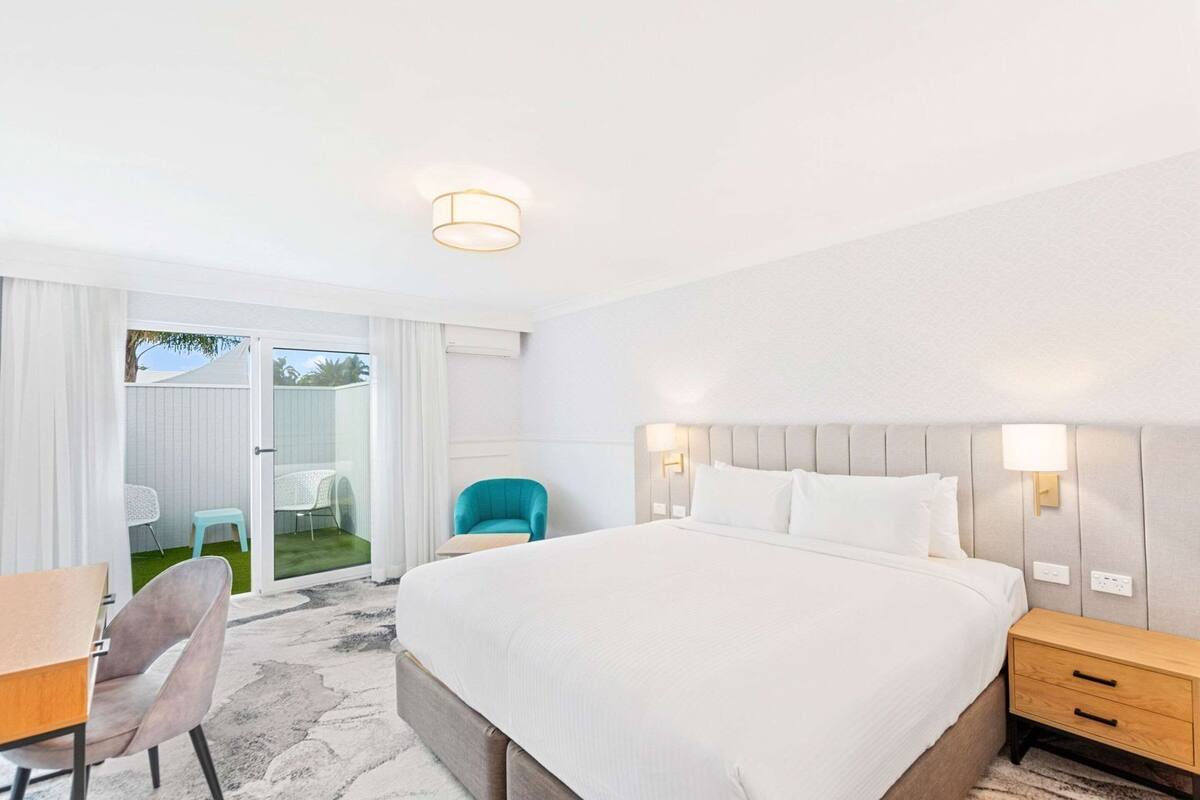 Une chambre d’hôtel équipée d’un lit, d’un bureau, d’une chaise, d’une table de chevet et offrant une vue sur l’extérieur.