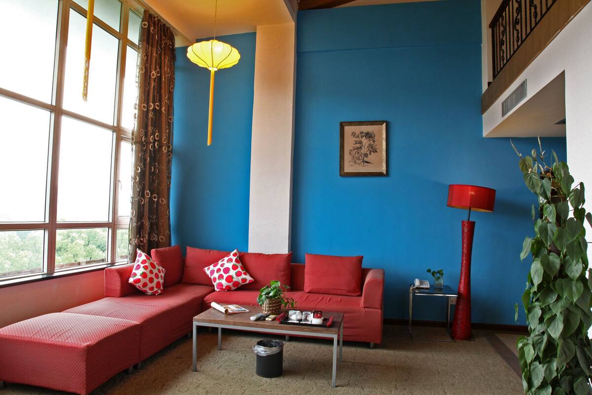 A living room with a red sofa, a coffee table, a red floor lamp, and a window with curtains.