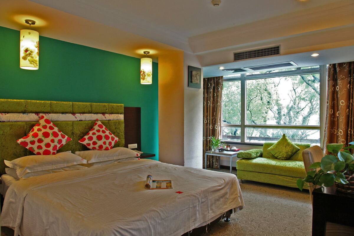 A hotel room with a large bed, a green sofa, and a window with curtains.