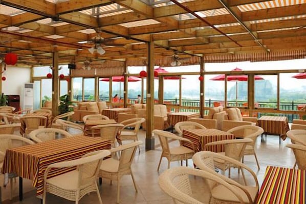 A spacious outdoor dining area with wicker furniture and red umbrellas, overlooking a scenic landscape.