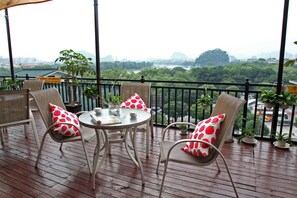 A balcony with wicker chairs and a table, surrounded by potted plants. - GuiLin Eva Inn Hotel (Guilin)