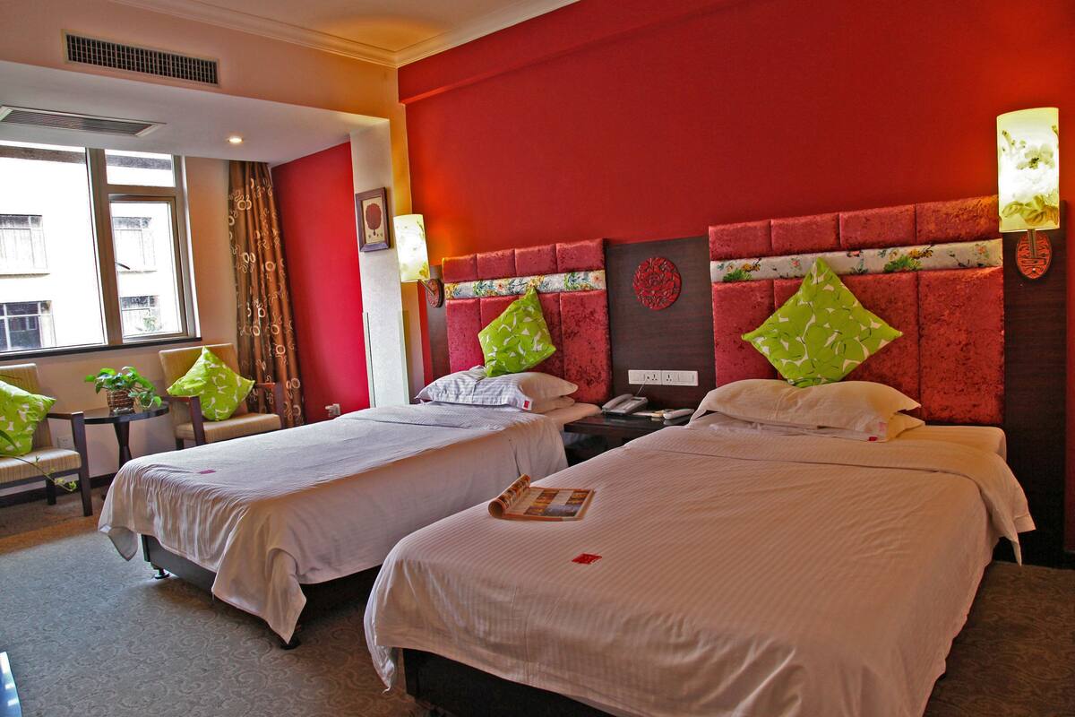 A hotel room with two beds, a small table with a plant, and a window with curtains.