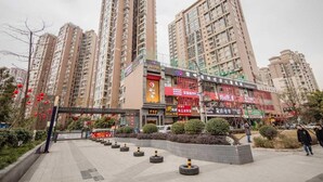 A high-rise residential building with multiple floors, a commercial area with various shops, and a landscaped area with bushes and a paved walkway. - Huaxi Angel Hotel - Chengdu (Chengdu)