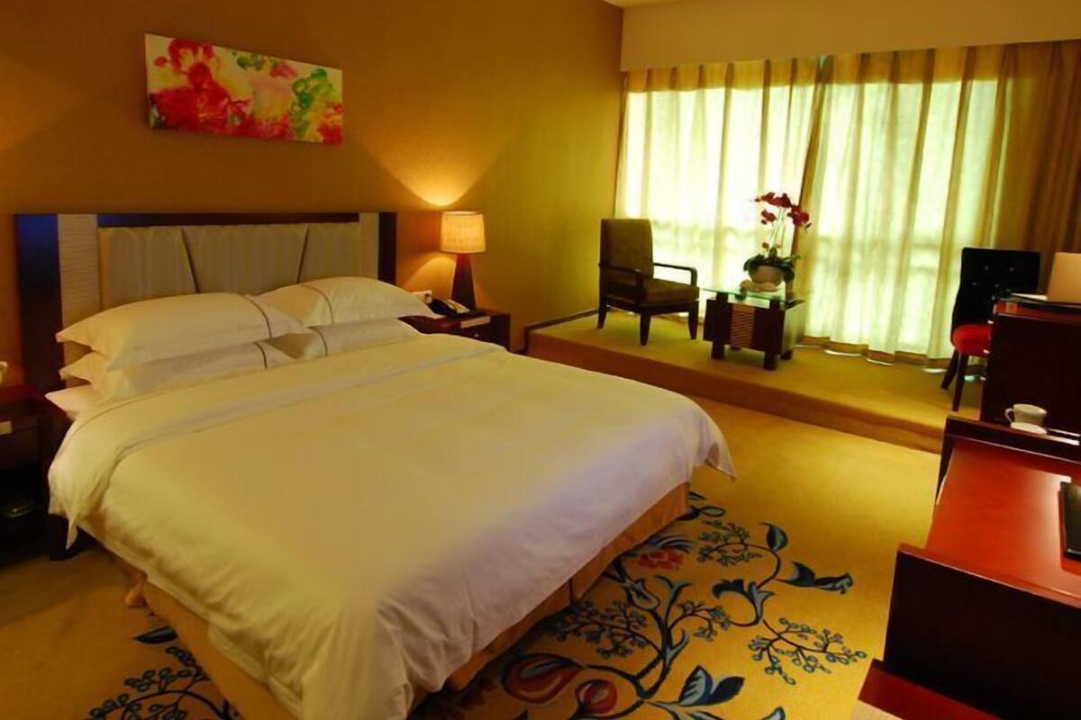 A hotel room with a large bed, a desk, a chair, a lamp, and a window with curtains.