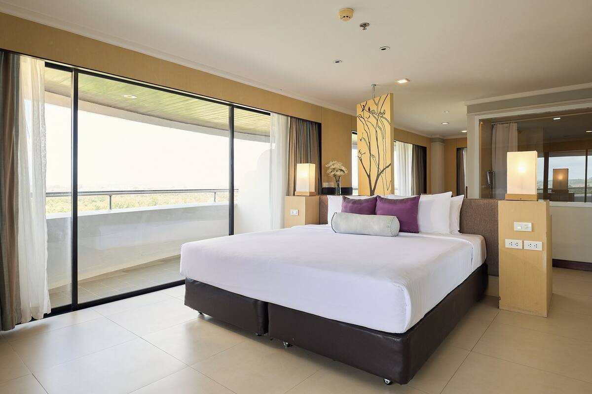 A hotel room with a large bed, a balcony with curtains, and a view of the outdoors.