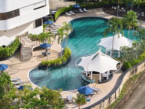 Zona de piscina en un resort con múltiples sillas de descanso, sombrillas y un diseño de piscina curvo.