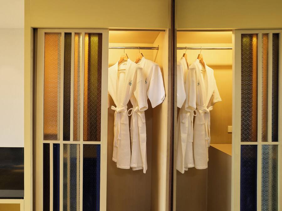 A room with a mirrored closet containing white robes hanging on a rod.