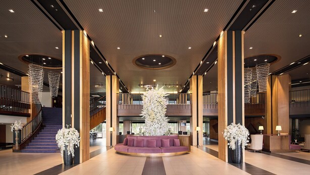 A spacious lobby with a central seating area, a staircase, and a reception desk.