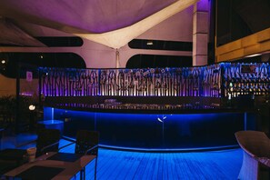 Zona de bar con mostrador curvo, iluminación azul y asientos.