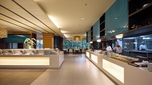 A modern hotel lobby with a reception desk, seating area, and a view of the kitchen.