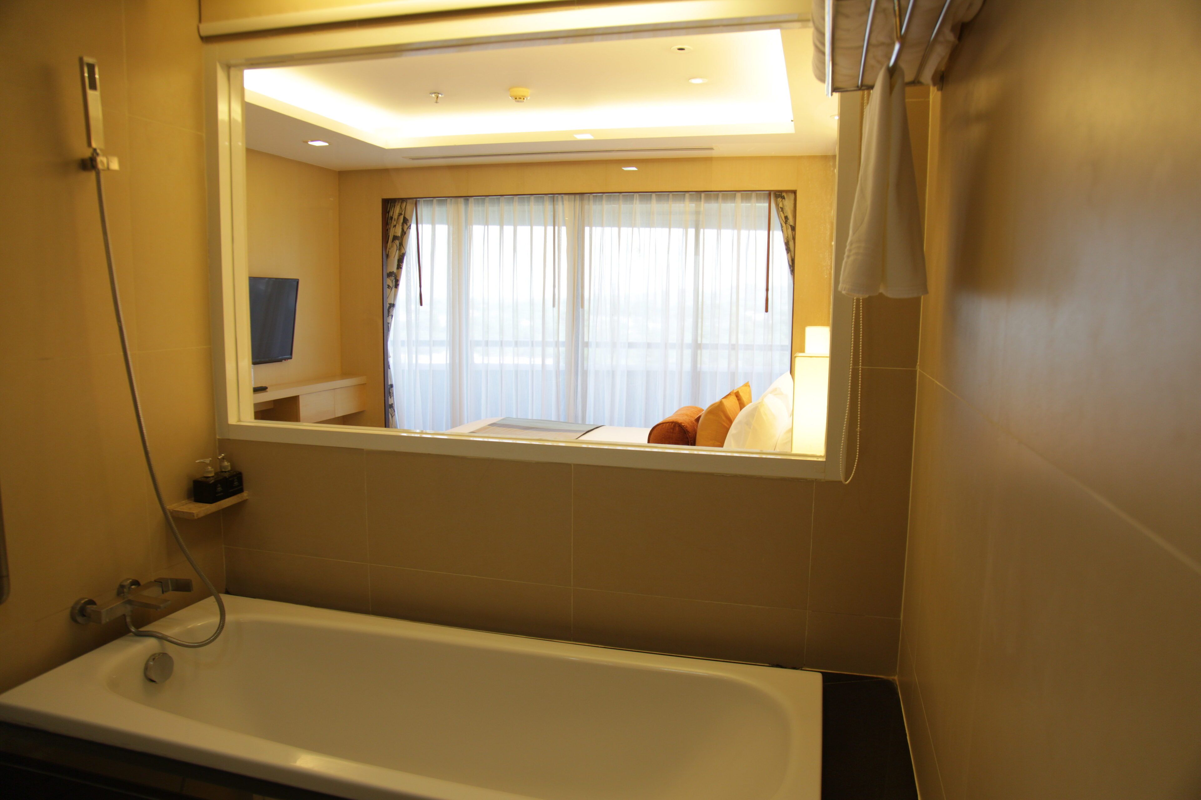 A modern bathroom with a bathtub, a window with curtains, and a mounted television.