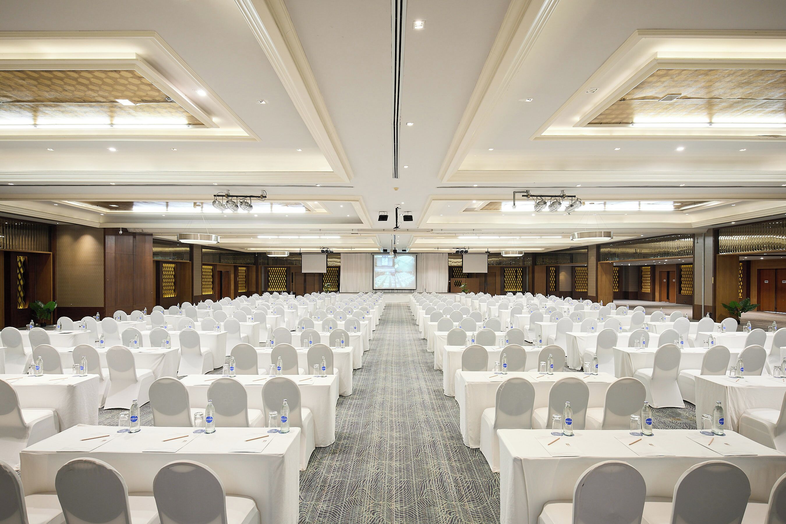 A large conference room with rows of tables and chairs, a carpeted floor, and a large screen at the front.