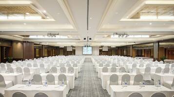 A large conference room with rows of tables and chairs, a carpeted floor, and a large screen at the front.