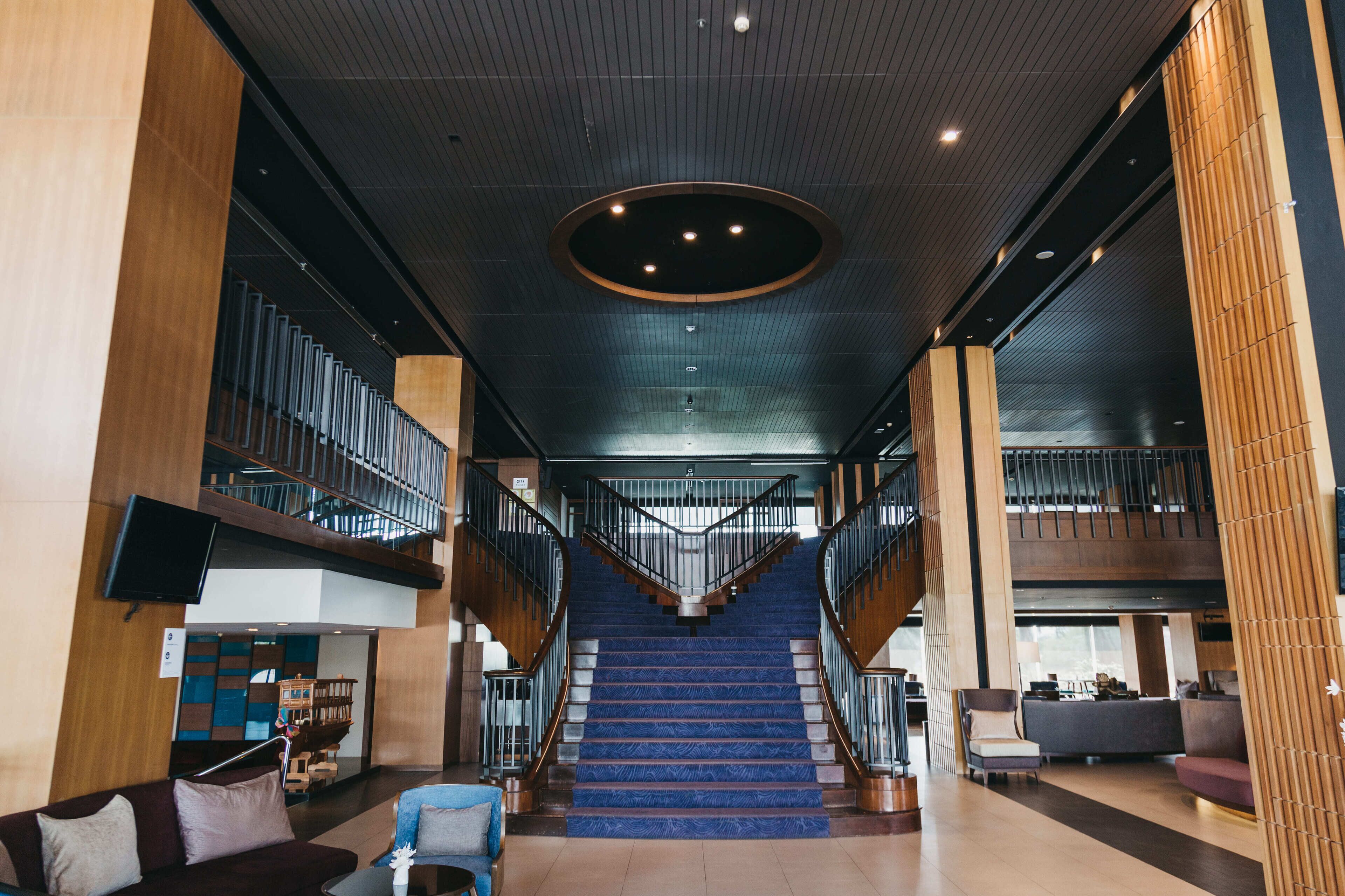 A spacious lobby with a central staircase, wooden columns, and a modern ceiling design.