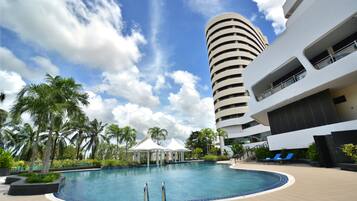 A swimming pool with lounge chairs, palm trees, and a modern building with balconies.