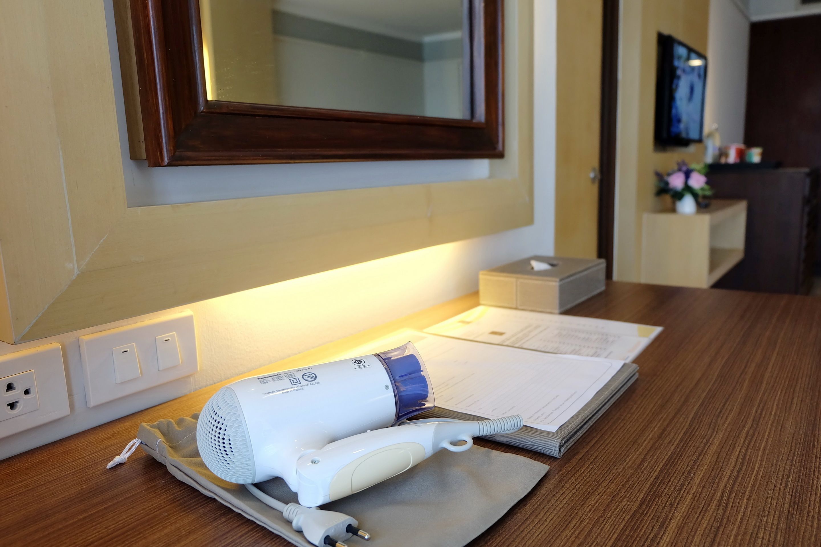 A hotel room with a wooden desk, a hairdryer, a charging cable, and a set of papers.