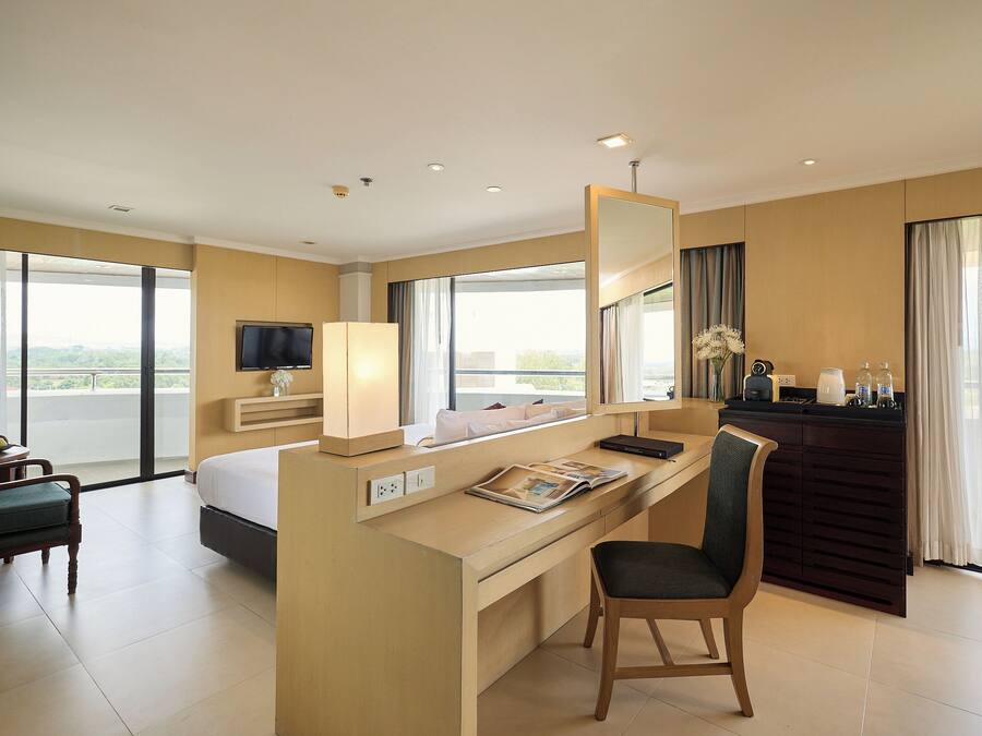 Habitación de hotel con cama, escritorio, silla, televisor y ventanas amplias con vista a la ciudad.