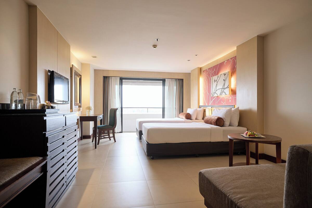 A hotel room with a bed, a desk, a chair, a TV, and a painting on the wall.