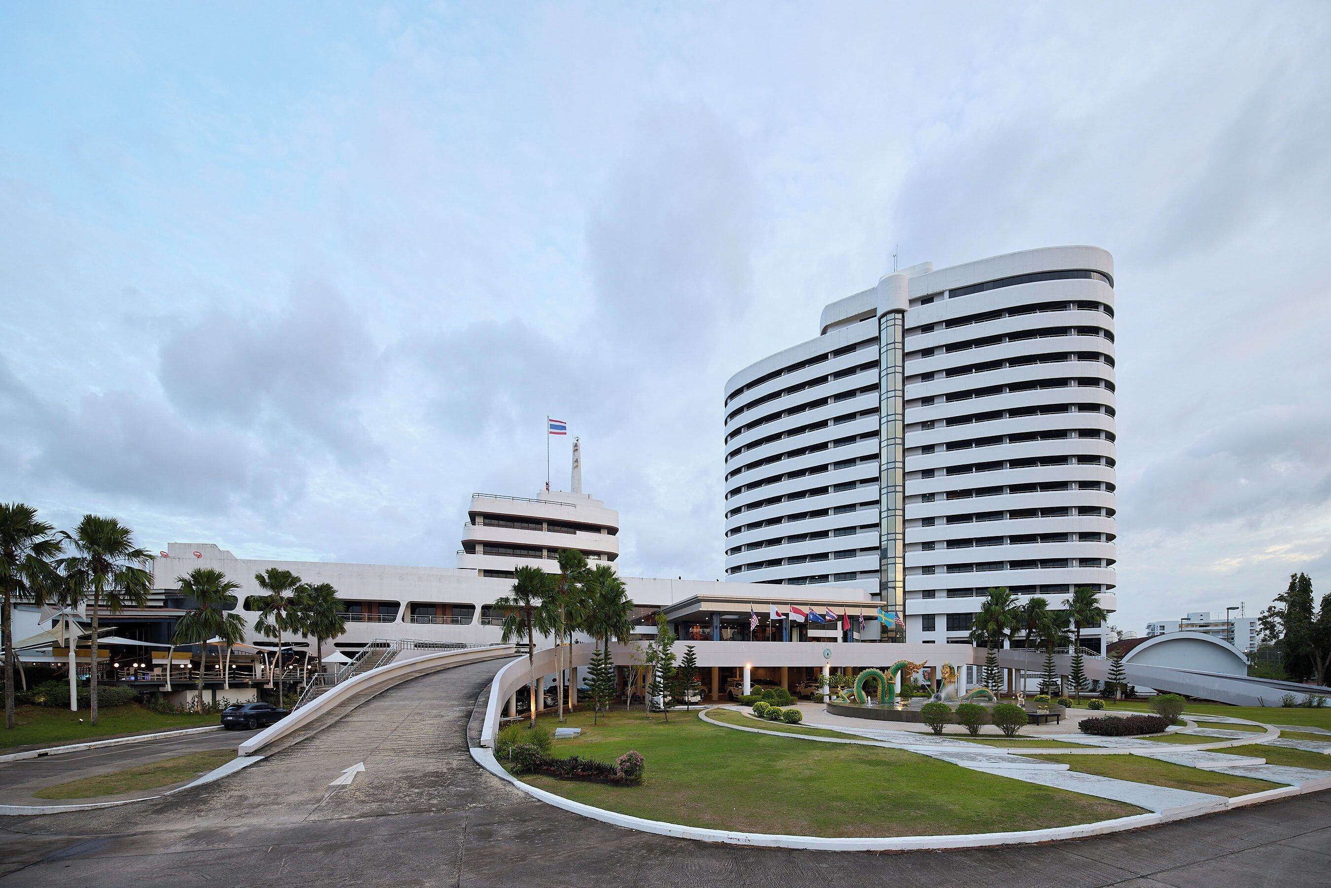 A modern hotel with a curved entrance, palm trees, and a flag.