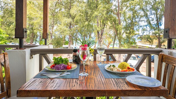 Une table en bois, dressée avec des assiettes remplies de nourriture, un verre de vin et un vase décoratif orné de fleurs.