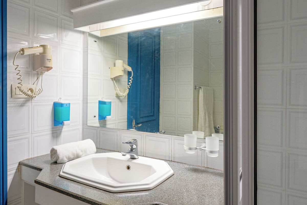 Een badkamer met een wit wastafel, een spiegel, een handdoek en een raam boven de spiegel.