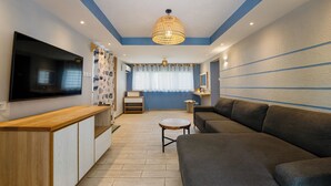Un salon moderne avec un téléviseur à écran plat, une table basse en bois, un canapé gris et un rideau à motifs.