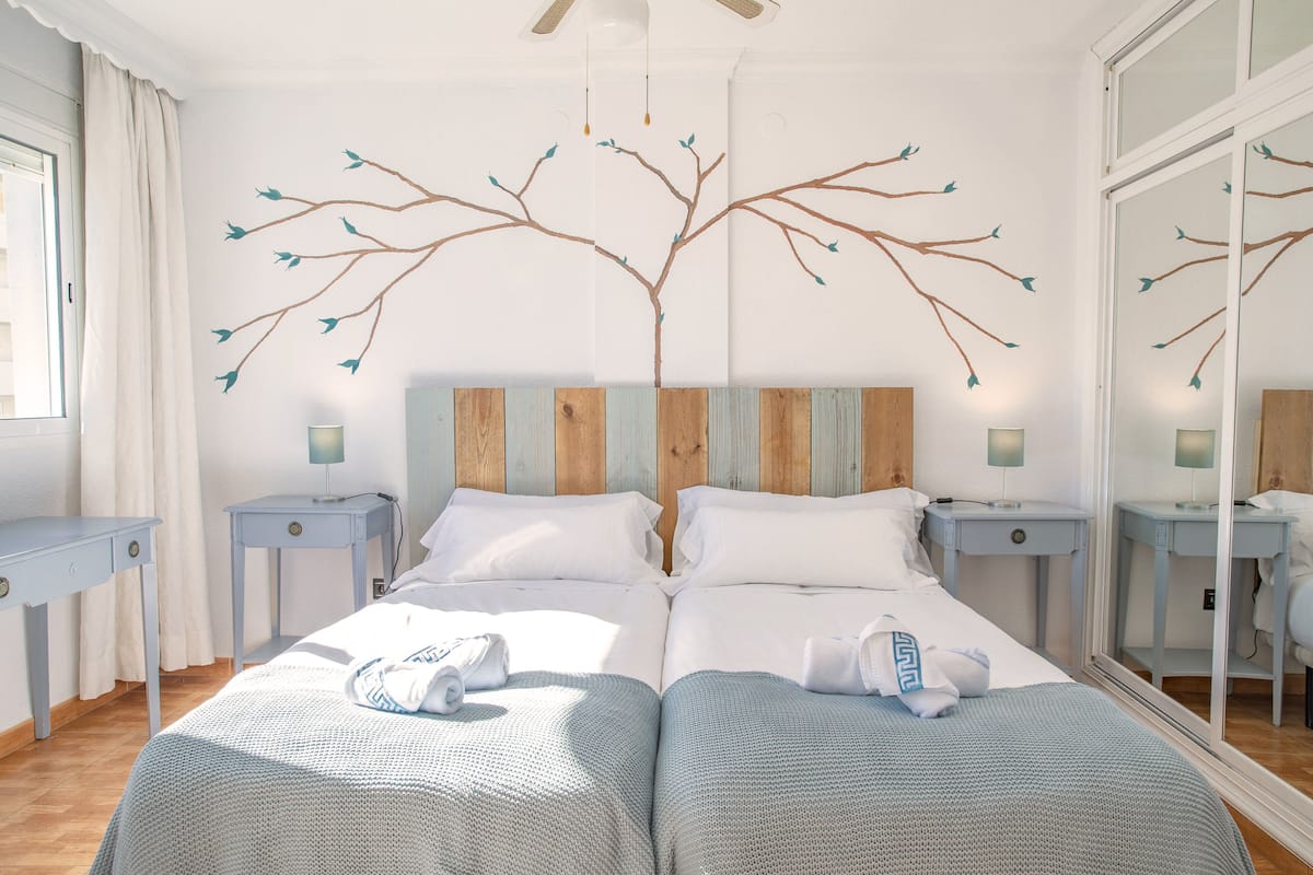 A double bed with a wooden headboard, two bedside tables, a mirror, and a window with curtains.