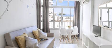 A living room with a sofa, a coffee table, a TV, and a balcony with a view.