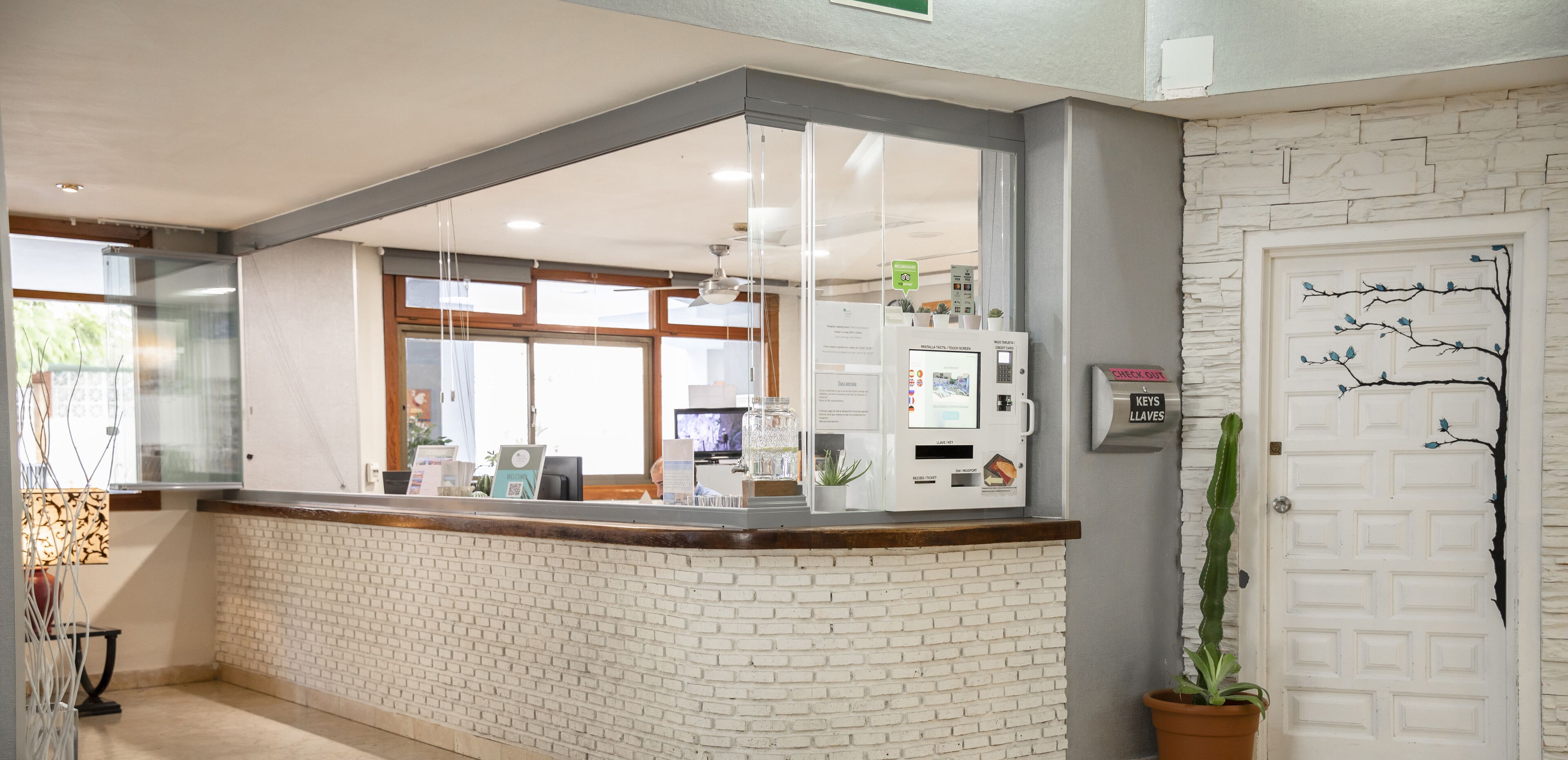 A reception area with a white brick counter, a glass partition, a digital kiosk, and a door with a decorative tree design.