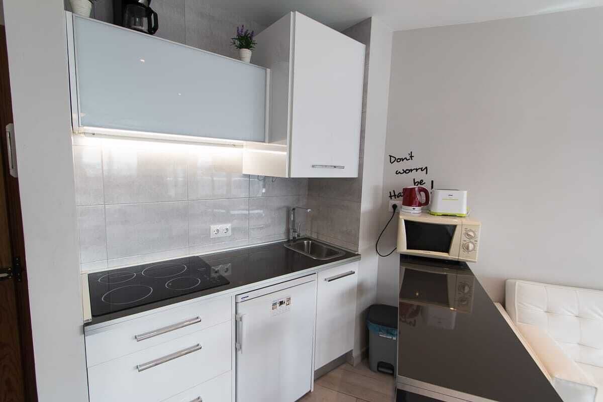 A compact kitchen with white cabinets, a black countertop, and a microwave on a shelf.