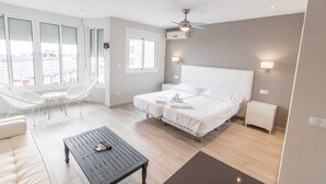 Een moderne hotelkamer met twee bedden, een balkon met witte stoelen, een kleine tafel en een plafondventilator.