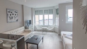 Een moderne woonkamer met een bank, een salontafel, een televisie en een balkon met witte stoelen.