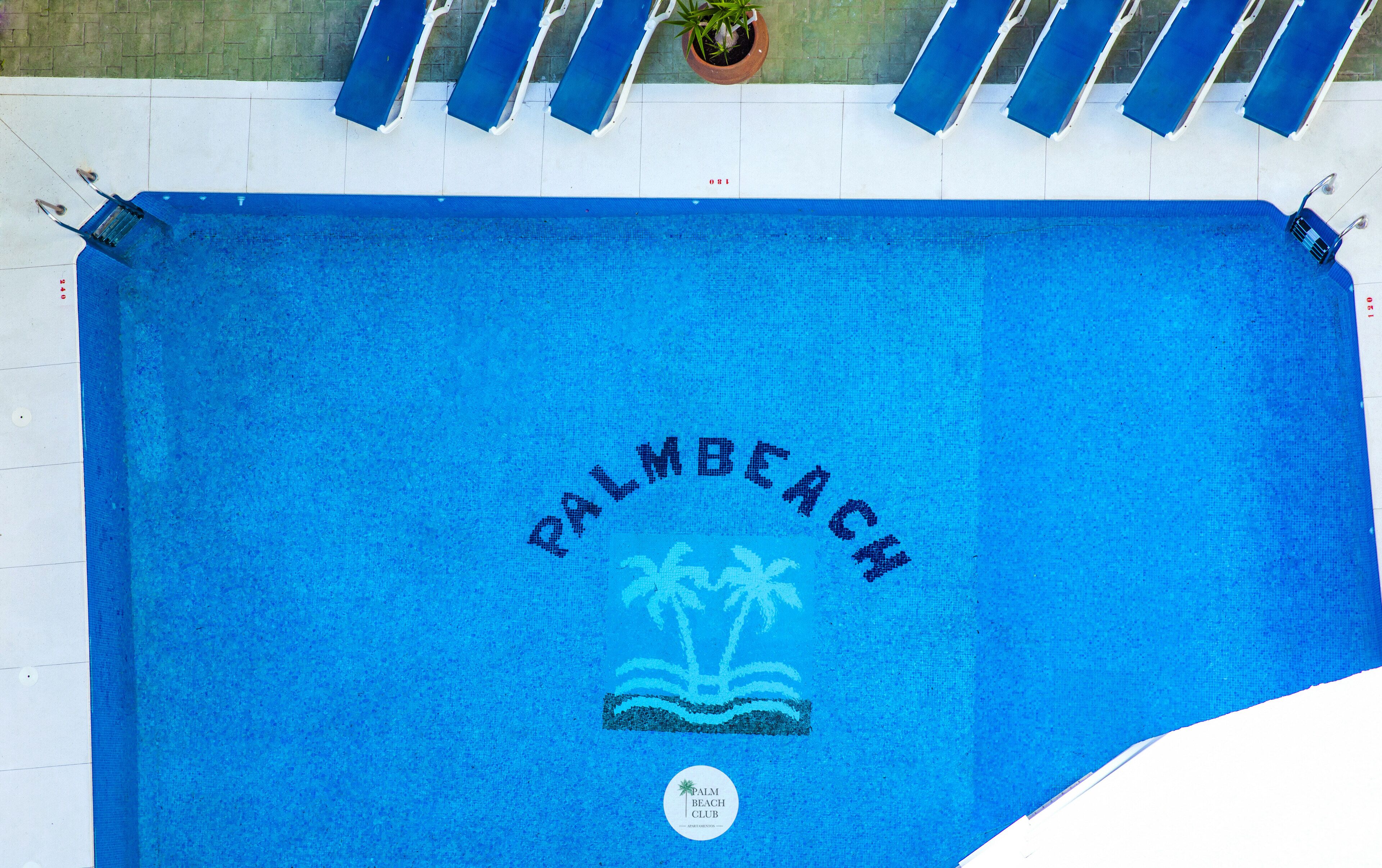 Une serviette bleue ornée d’un logo représentant « Palm Beach » et des palmiers, ainsi que d’une image d’un palmier et de l’inscription « Palm Beach Club ».