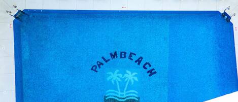 Une serviette bleue ornée d’un logo représentant « Palm Beach » et des palmiers, ainsi que d’une image d’un palmier et de l’inscription « Palm Beach Club ».